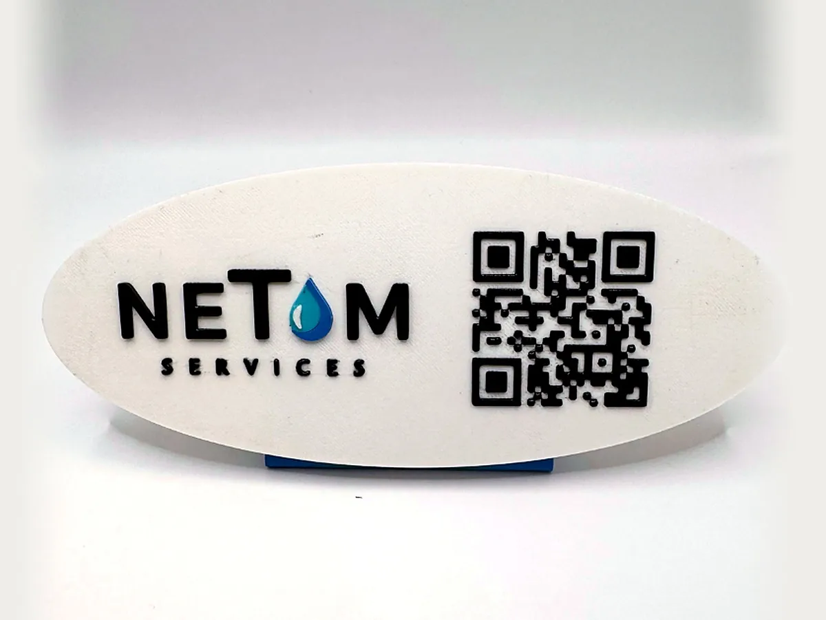Plaque ovale blanche avec le logo NETOM Services et un QR code noir en relief, sur un pied bleu